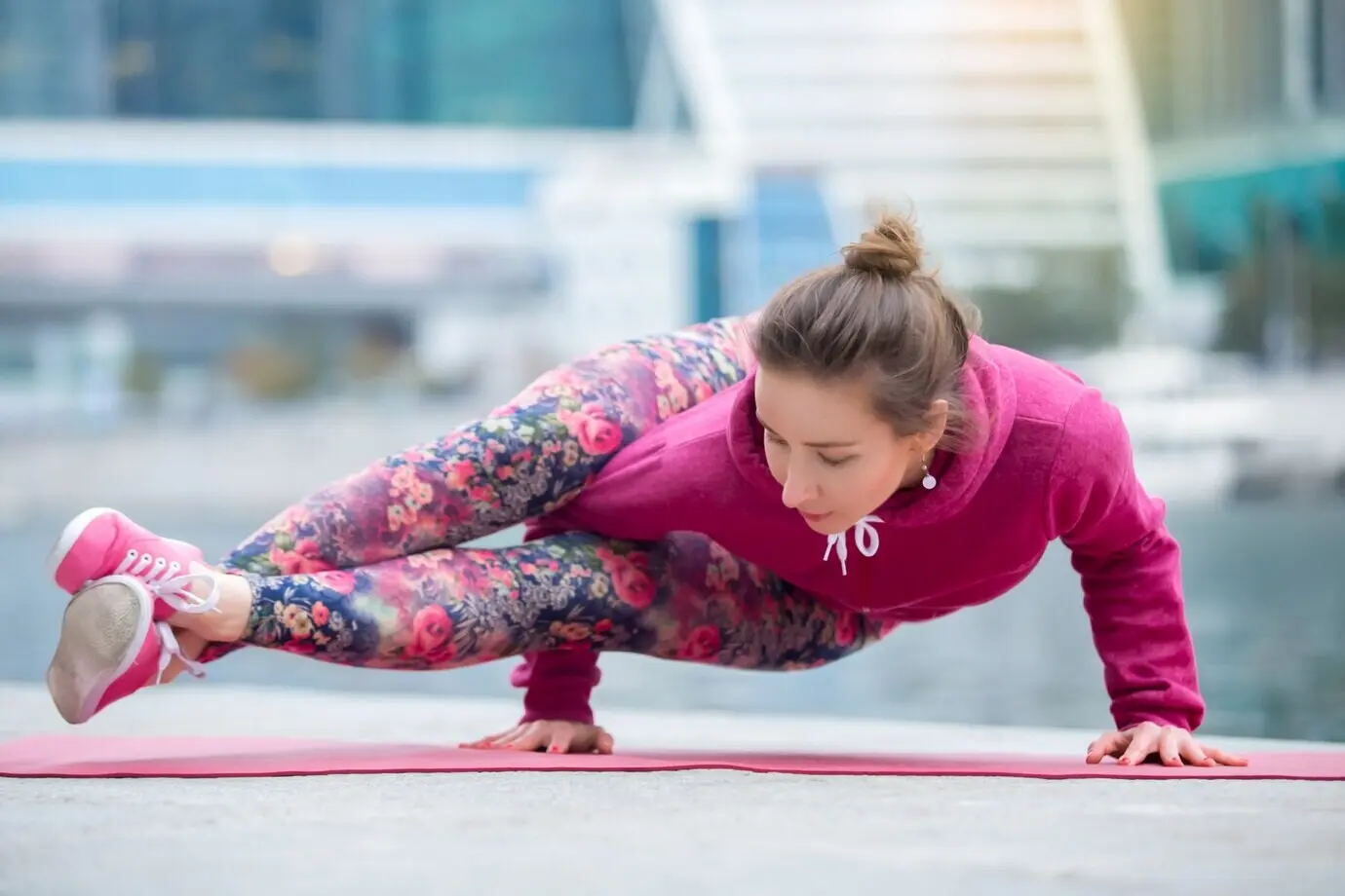 Junge Frau in der Astavakrasana-Haltung mit Stadt und Fluss im Hintergrund
