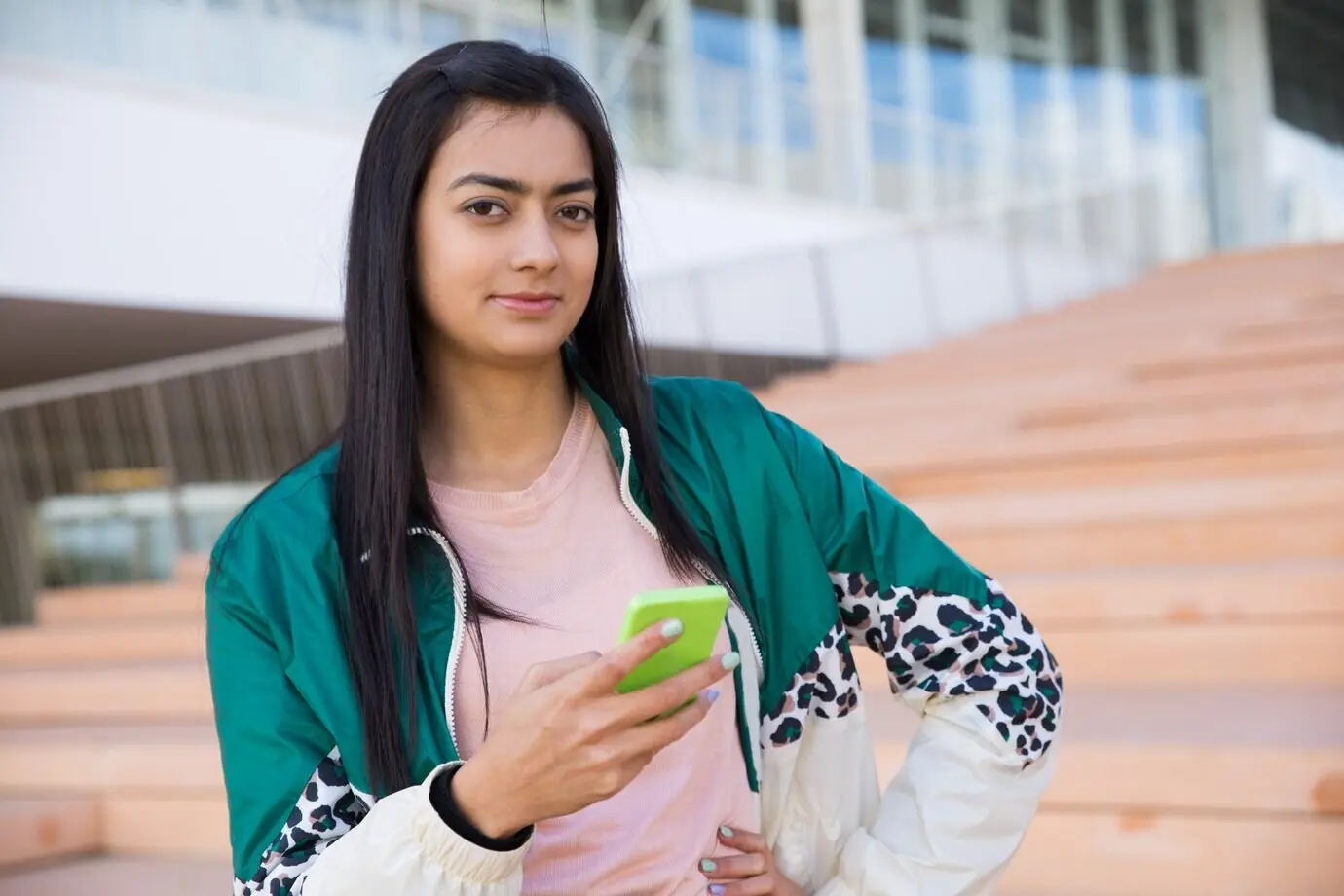 Hübsche Frau auf einer Treppe, die in die Kamera blickt und ein Handy in der Hand hält.
